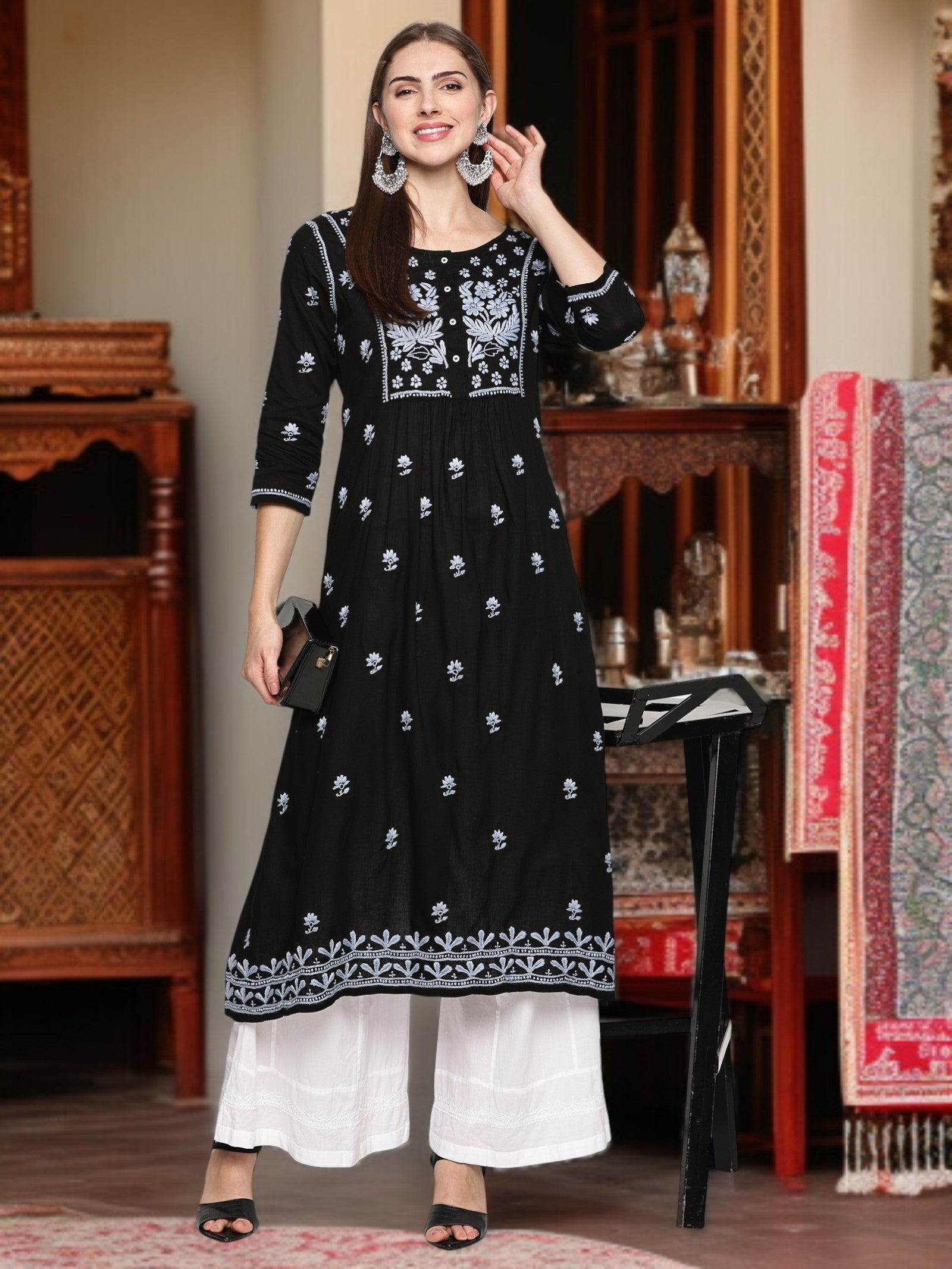 Woman wearing a black and embroidered dress in an indoor setting.