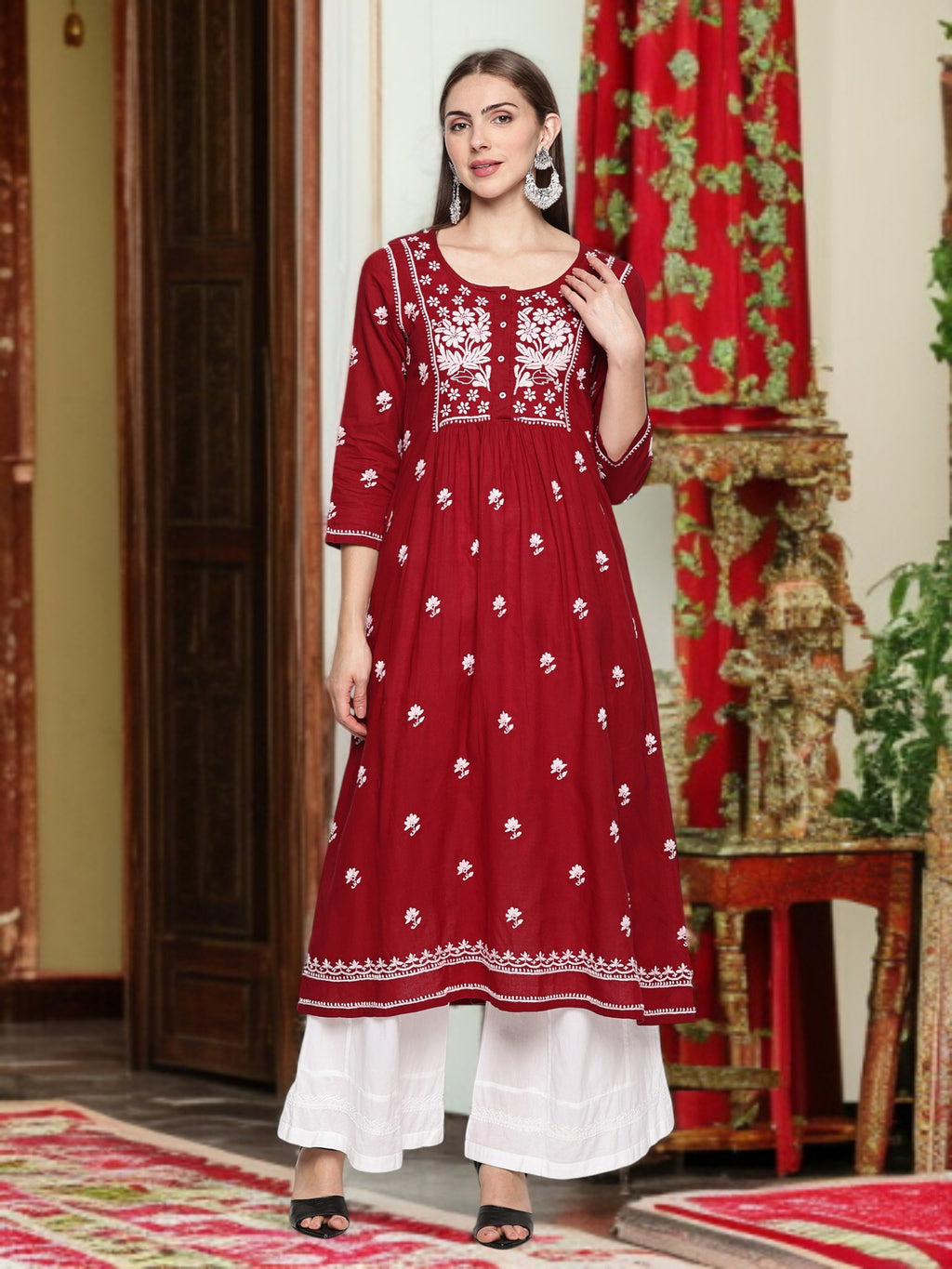 A woman wearing a maroon and embroidered traditional outfit in a decorated room.