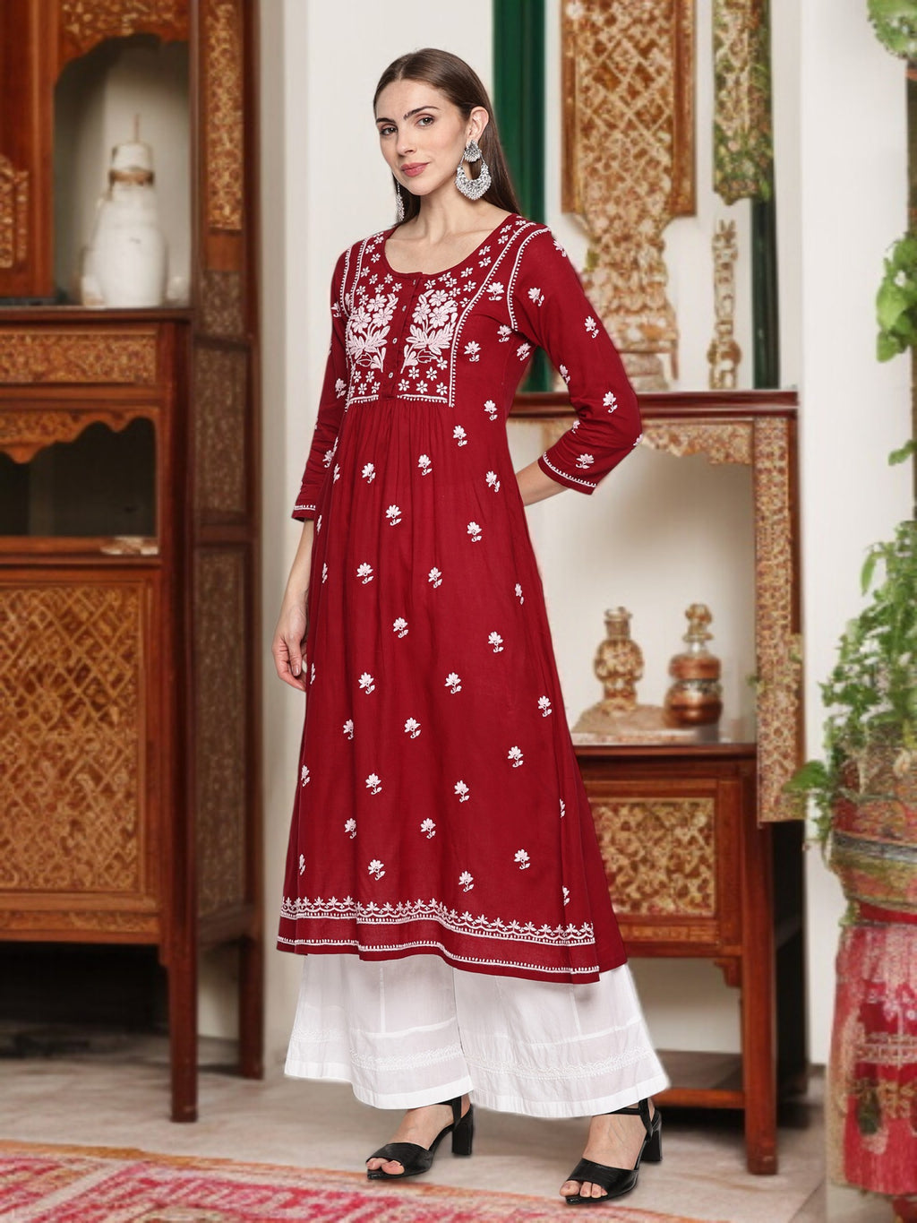 A woman wearing a maroon and embroidered dress in an ornate room.
