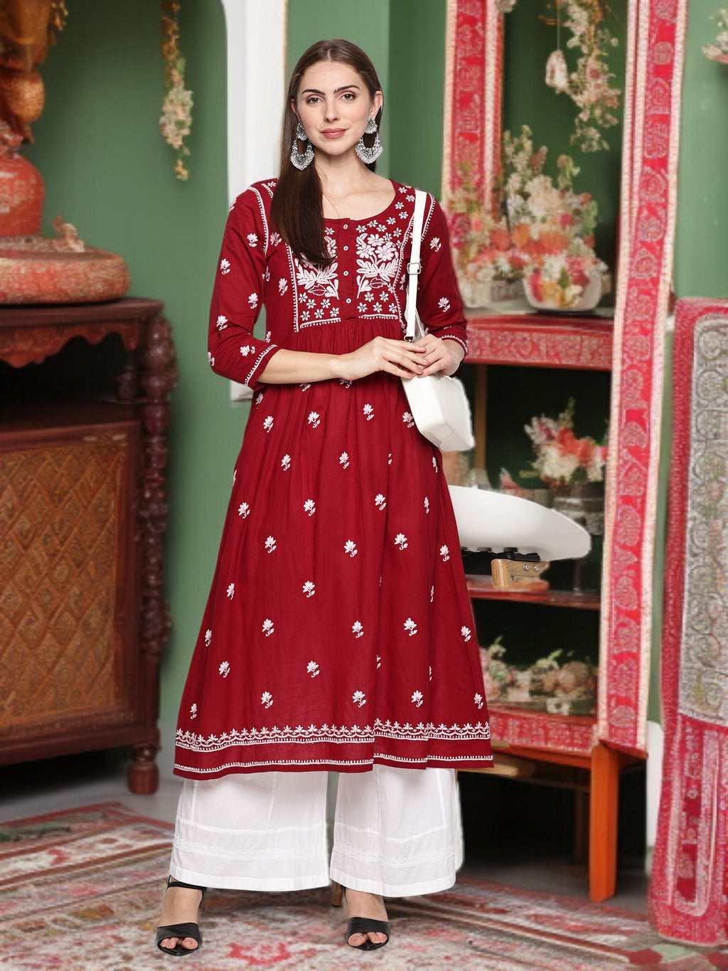 A woman wearing a maroon and embroidered traditional outfit in a decorated room.