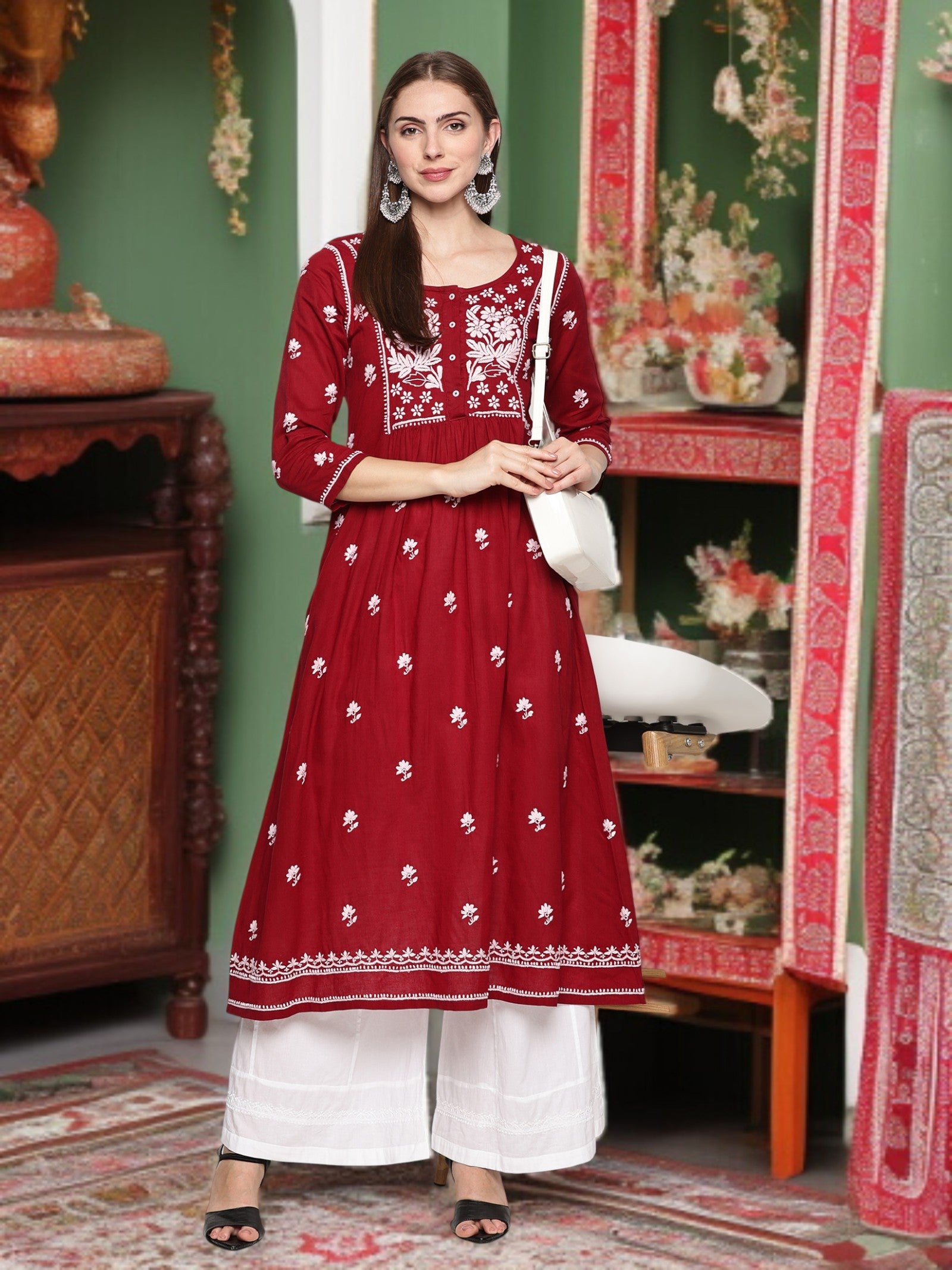 A woman wearing a maroon and embroidered traditional outfit in a decorated room.