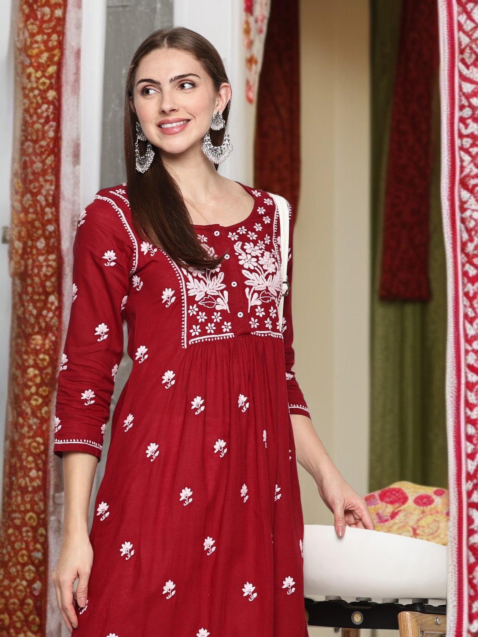 A woman wearing a maroon embroidered dress in a decorated room.