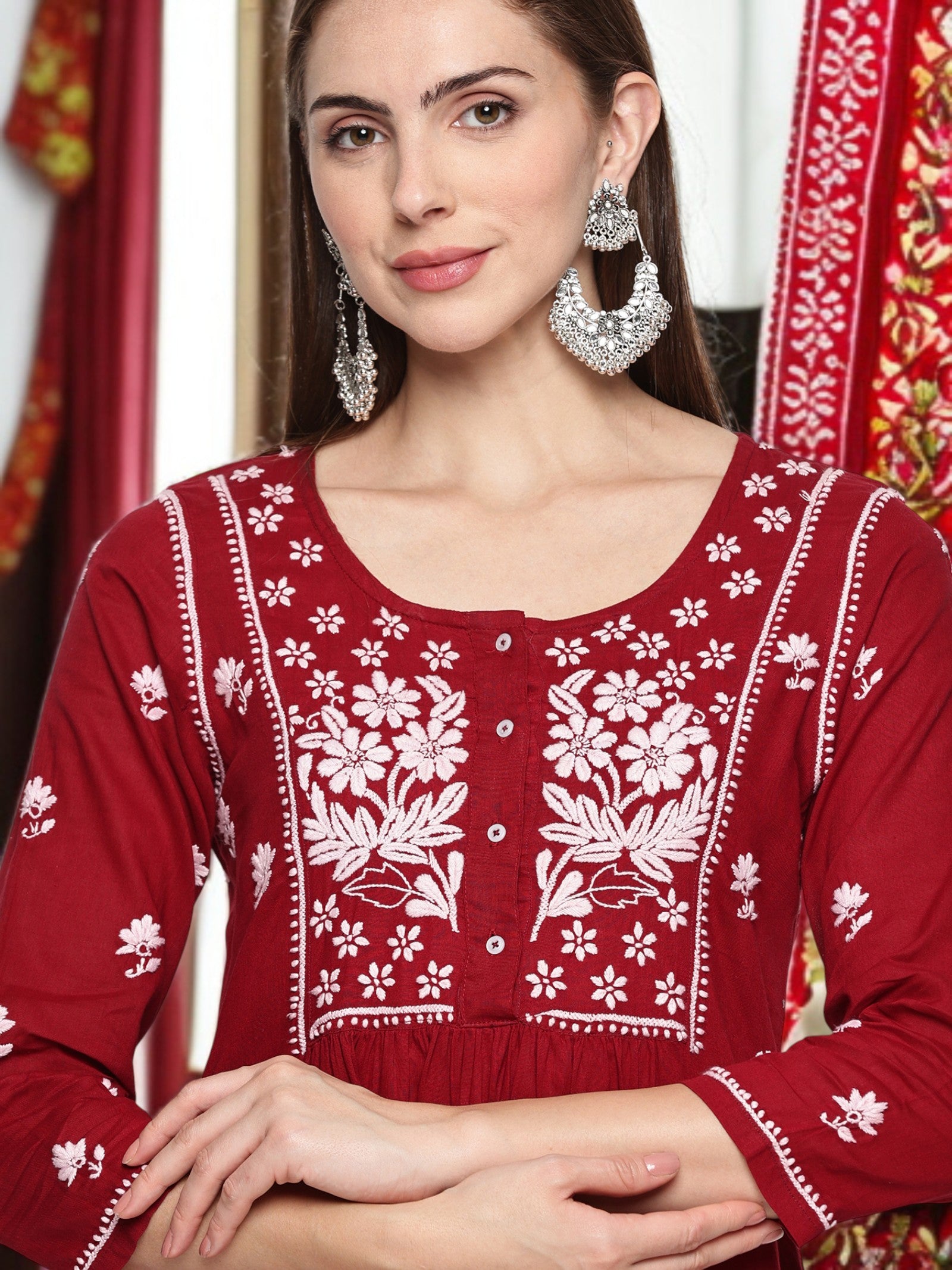 Woman wearing a maroon traditional outfit with  floral embroidery against a colorful background