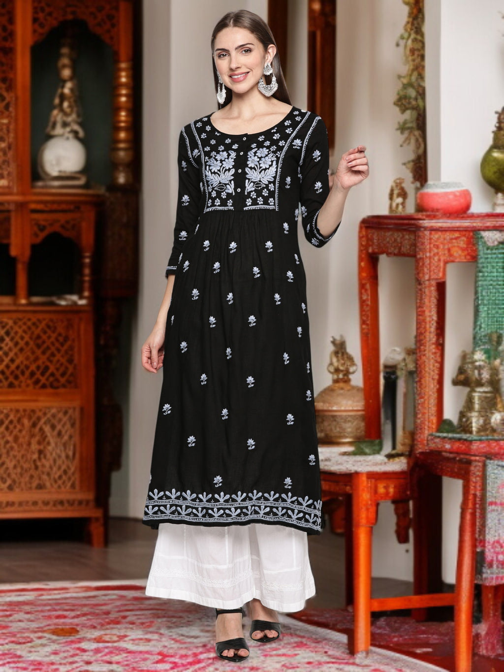 A woman wearing a black embroidered dress in an indoor setting.