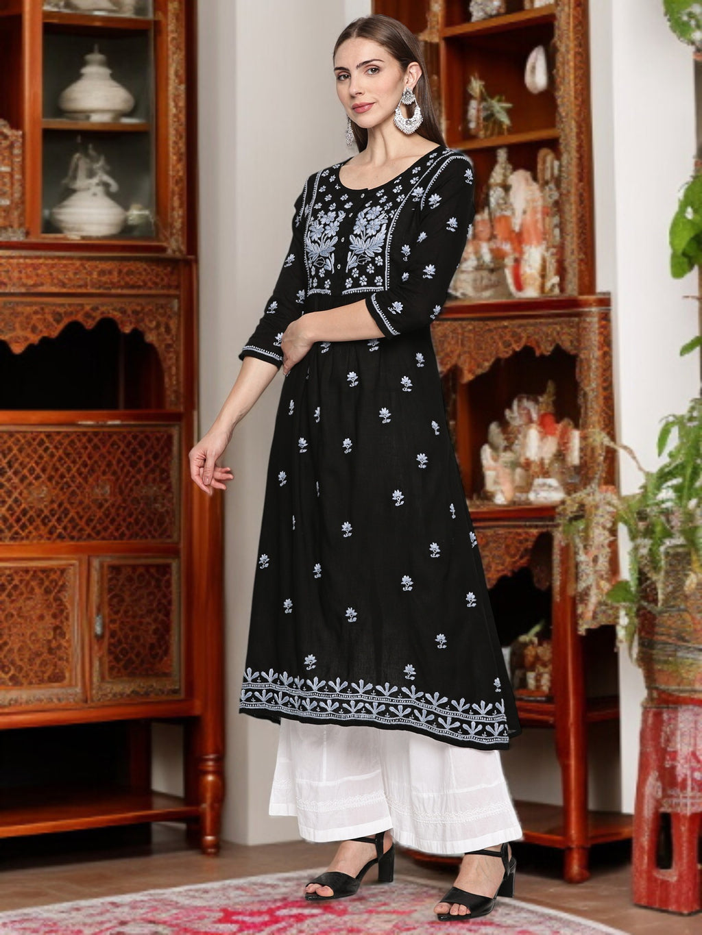 A woman wearing a black embroidered outfit in a decorated room.