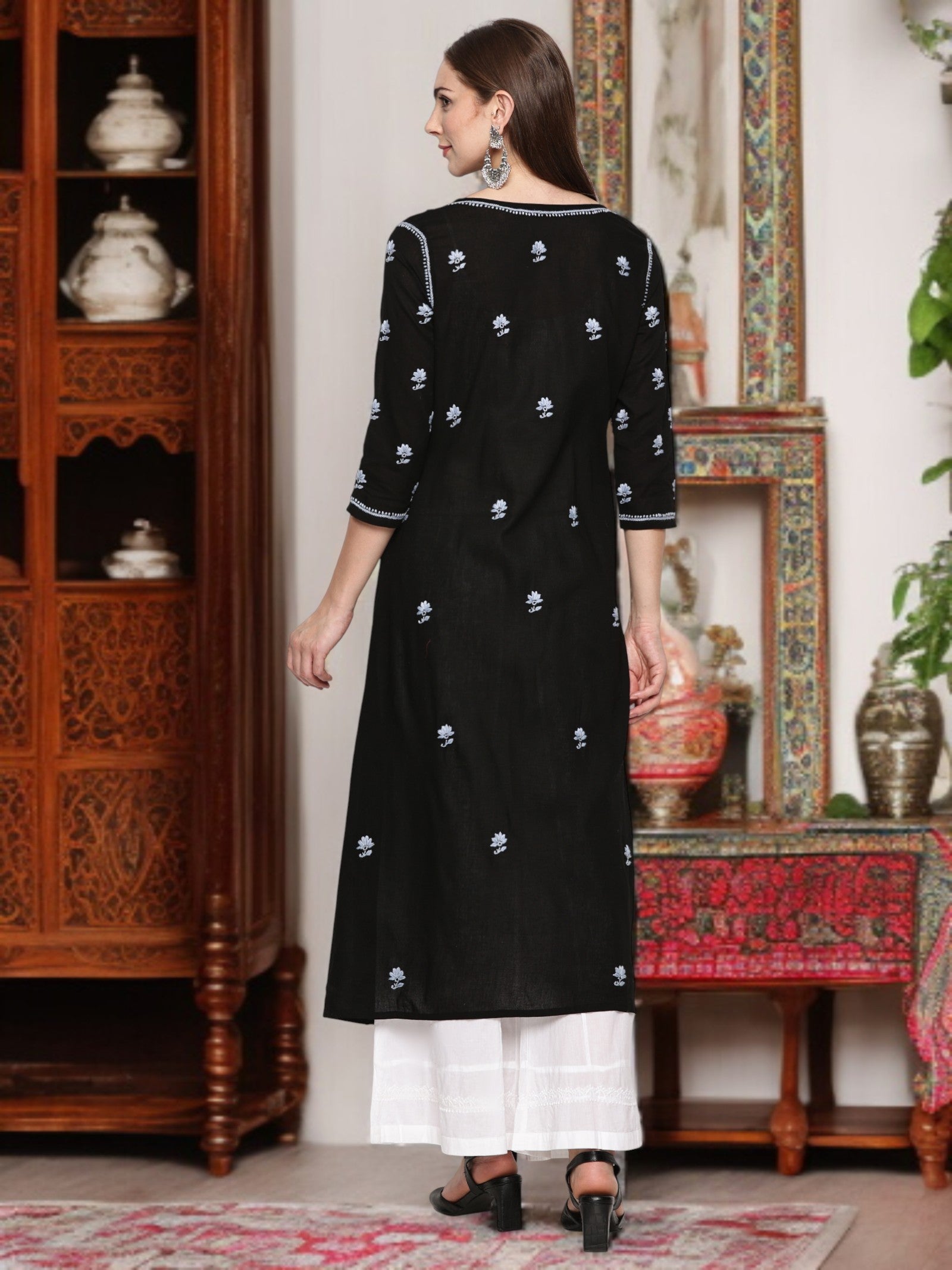 A woman wearing a black kurta with patterns in a decorated room.