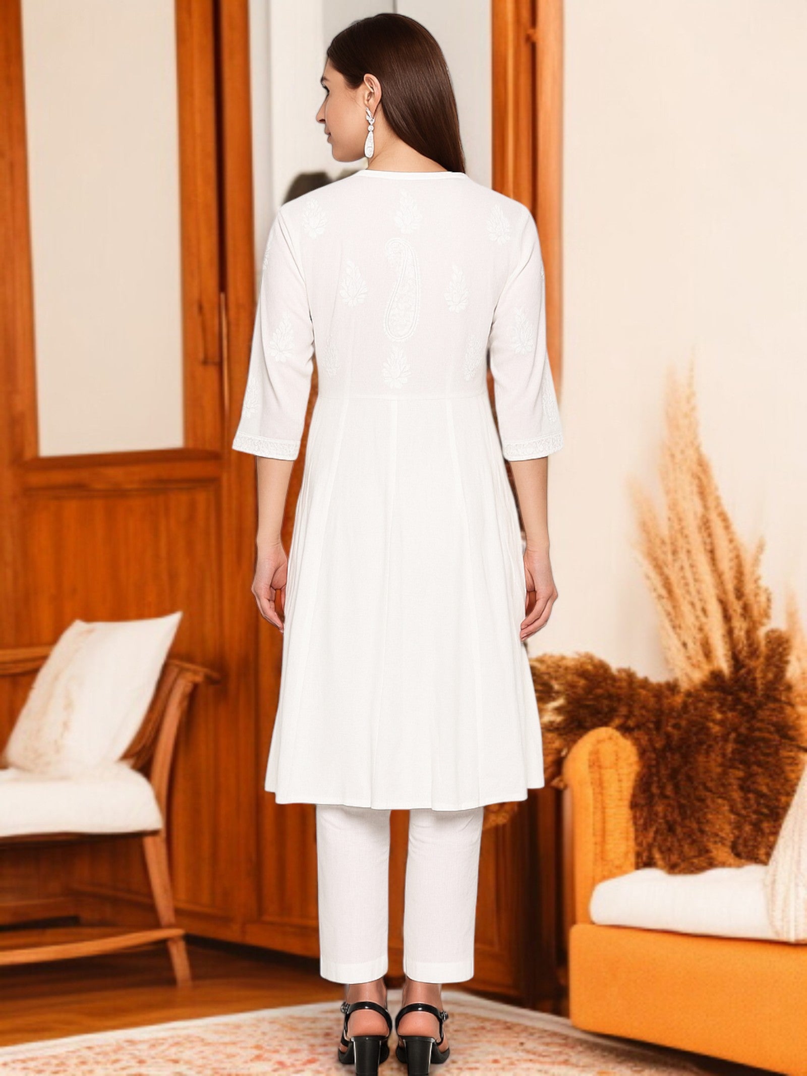 Woman wearing a white outfit in a room with wooden furniture and an orange chair.