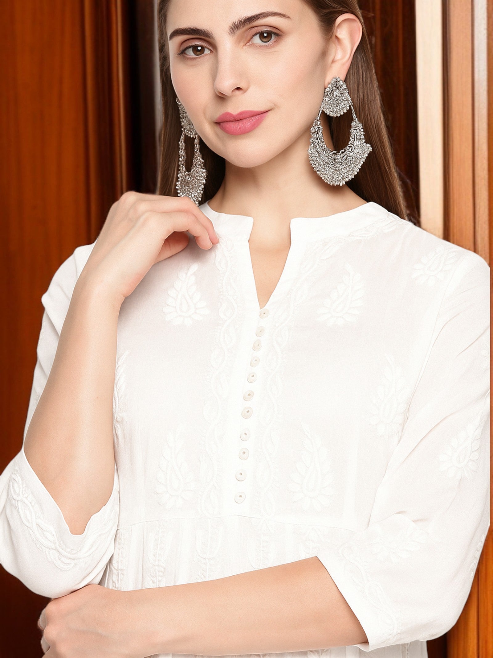 Woman wearing a white blouse with silver hoop earrings against a wooden background